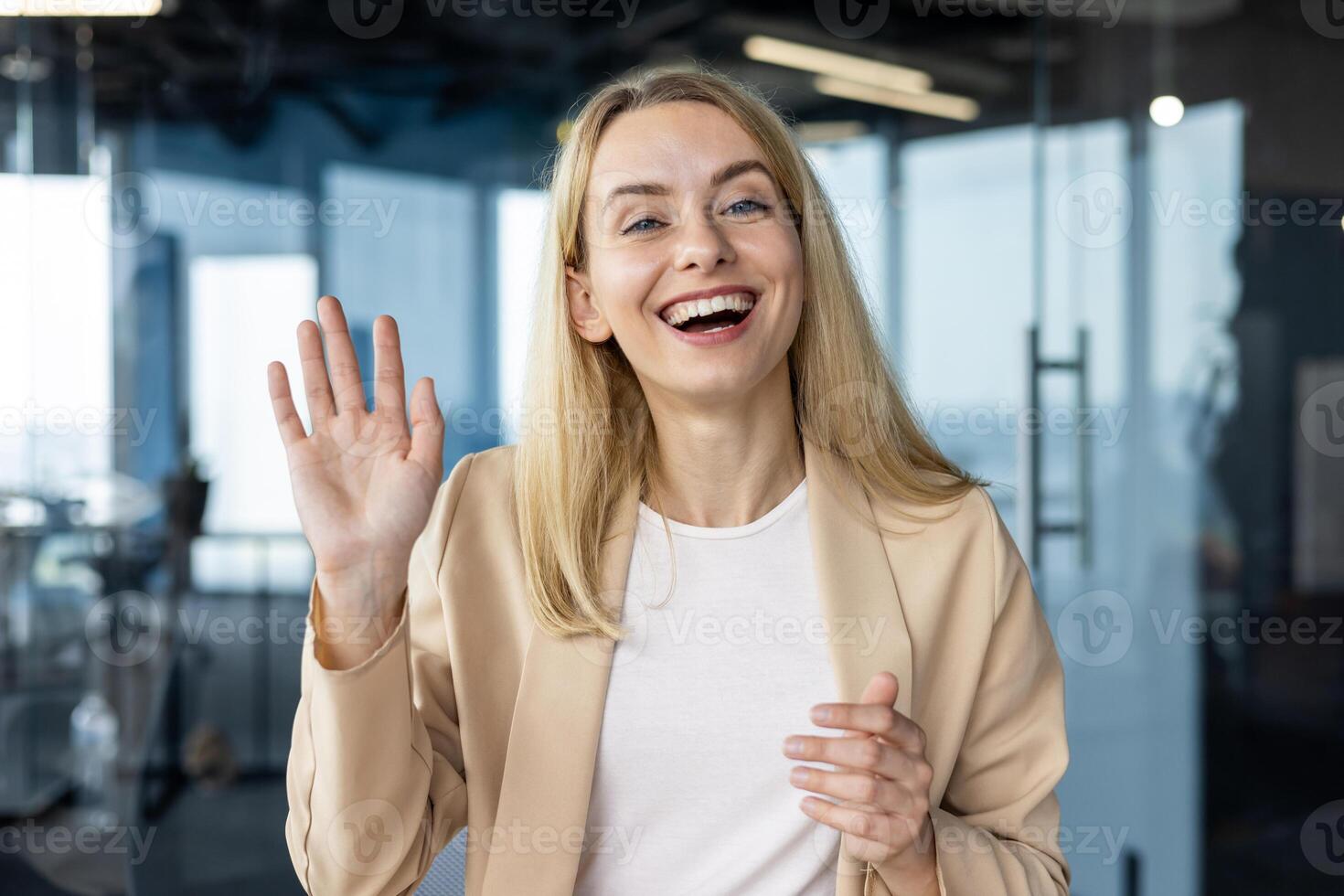 Smiling businesswoman waving hello during a call in a contemporary office setting. Perfect image depicting remote communication and business engagement. photo