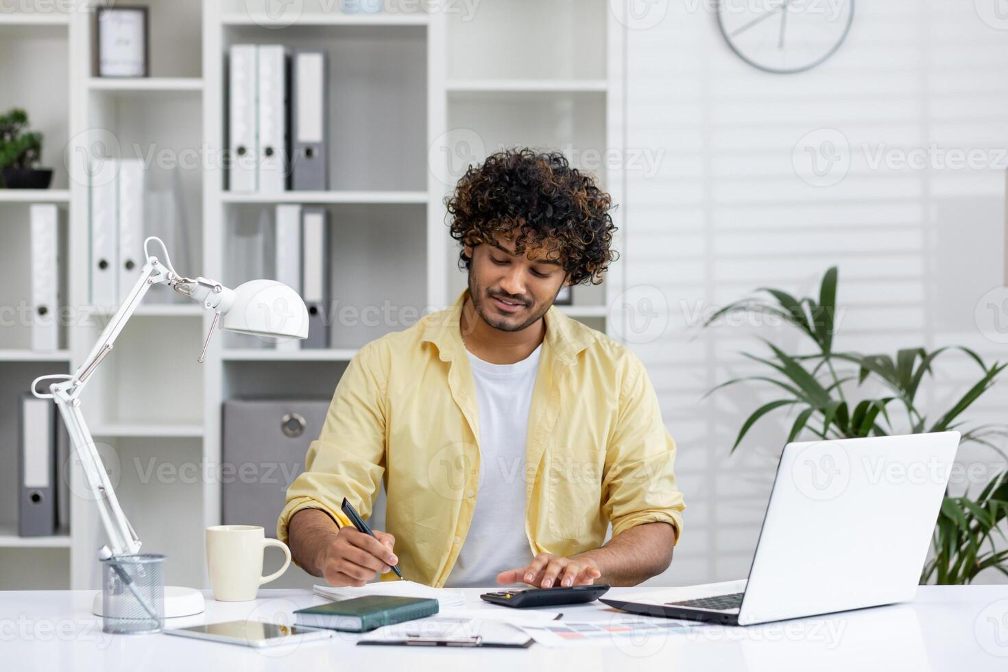 Young professional uses laptop, documents, and calculator while working from home in a modern, well-organized office. photo