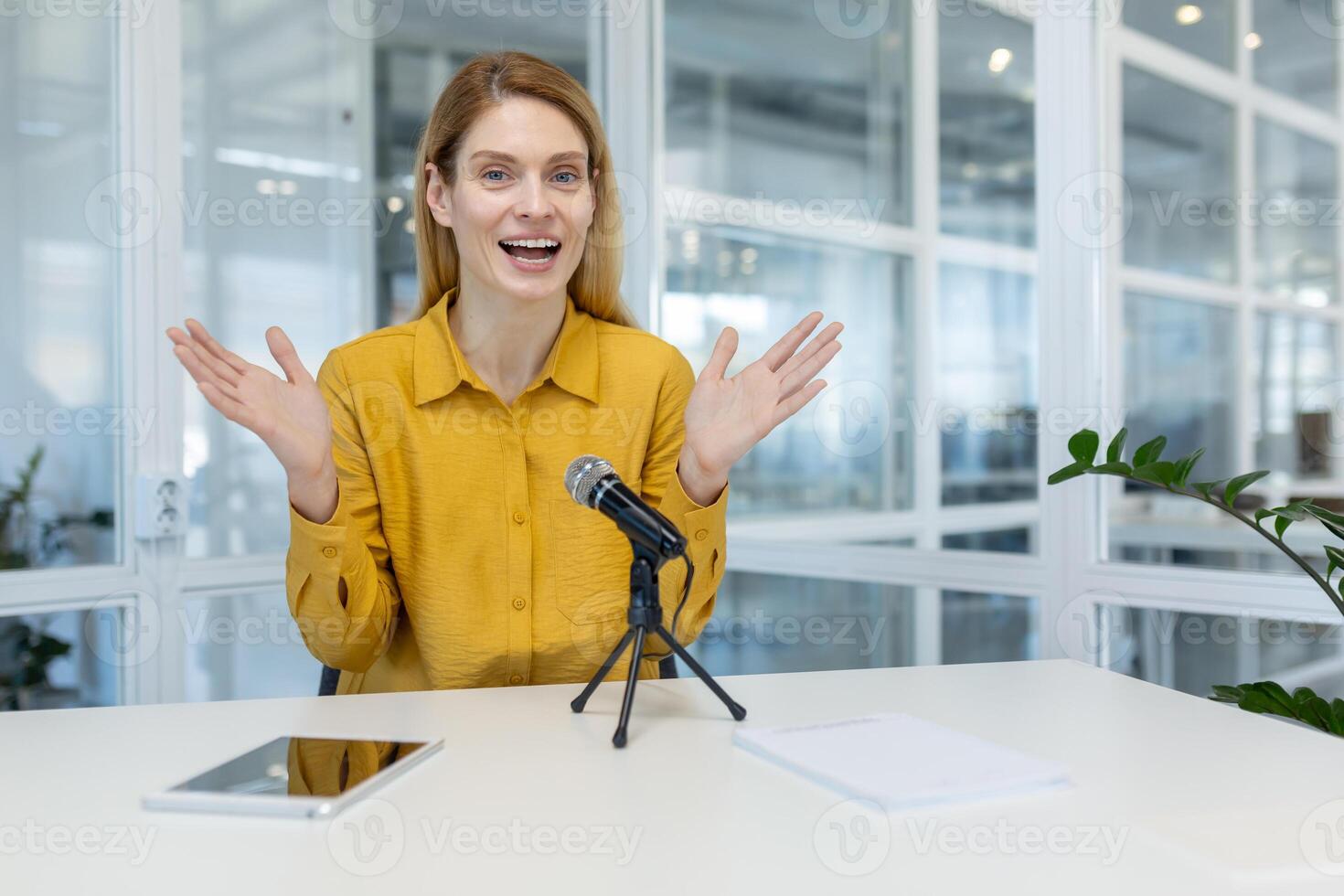 Smiling woman in a yellow shirt hosting a podcast or call in a bright, modern office. Professional communication during a recording or virtual meeting. photo