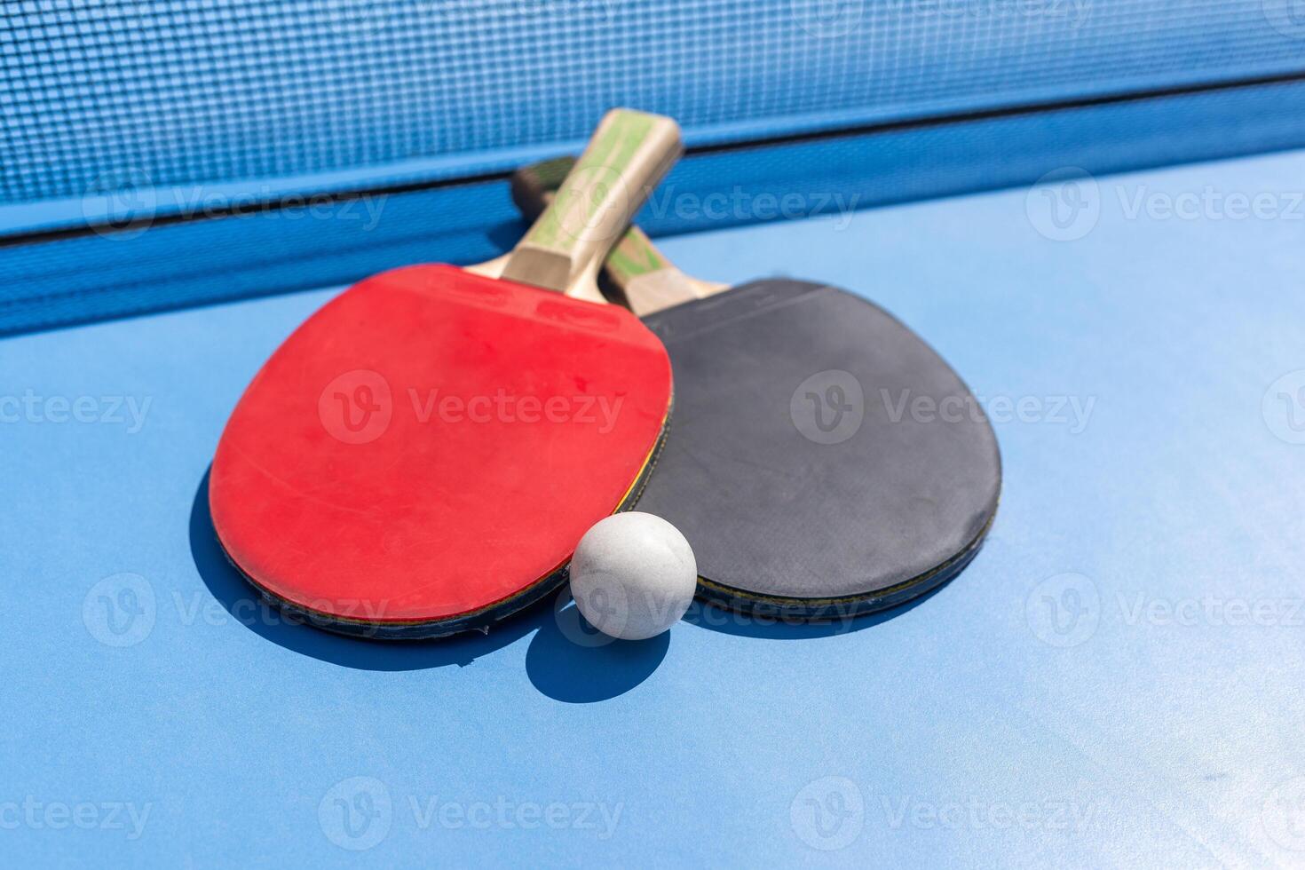 Two table tennis or ping pong rackets and ball on blue table with net photo