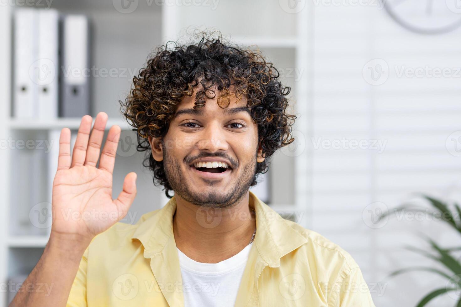Smiling young man waving during a call. Friendly and happy interaction in a home office setting. photo