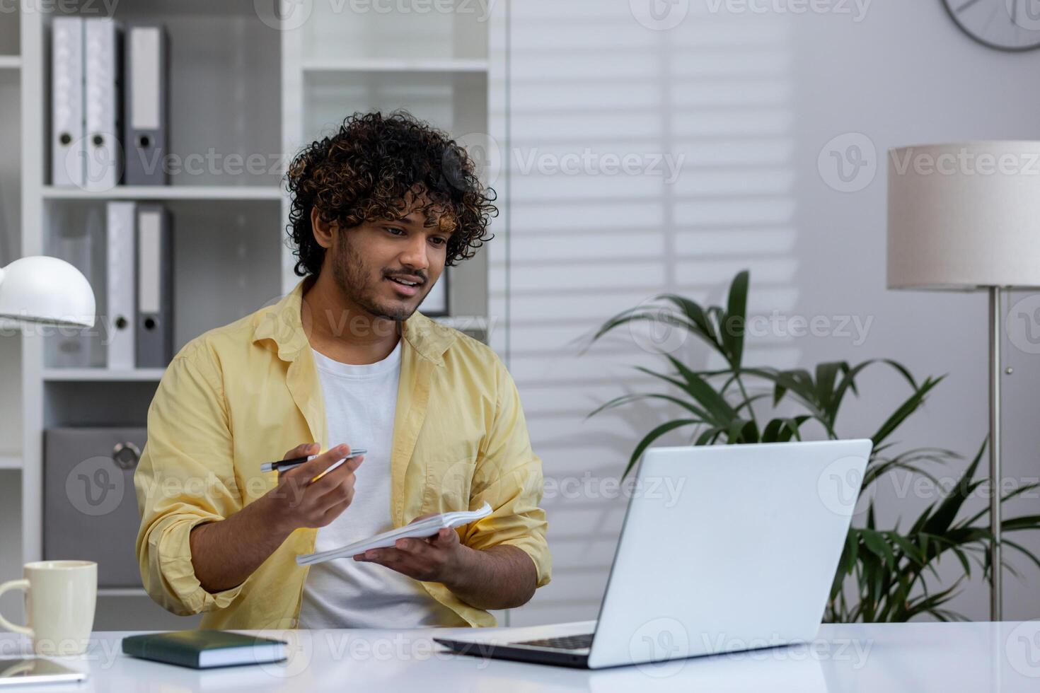 Young man taking notes while engaging in an online course. Learning remotely at home with a laptop in a modern workspace. photo