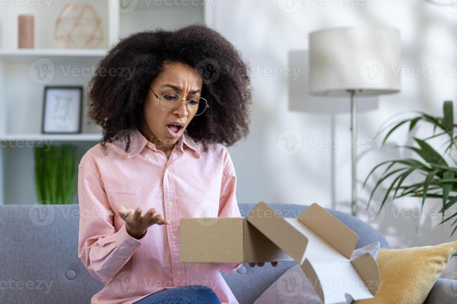 Woman with a surprised and puzzled expression opening an empty cardboard box at home. Concept of expectation, disappointment, and online shopping. photo