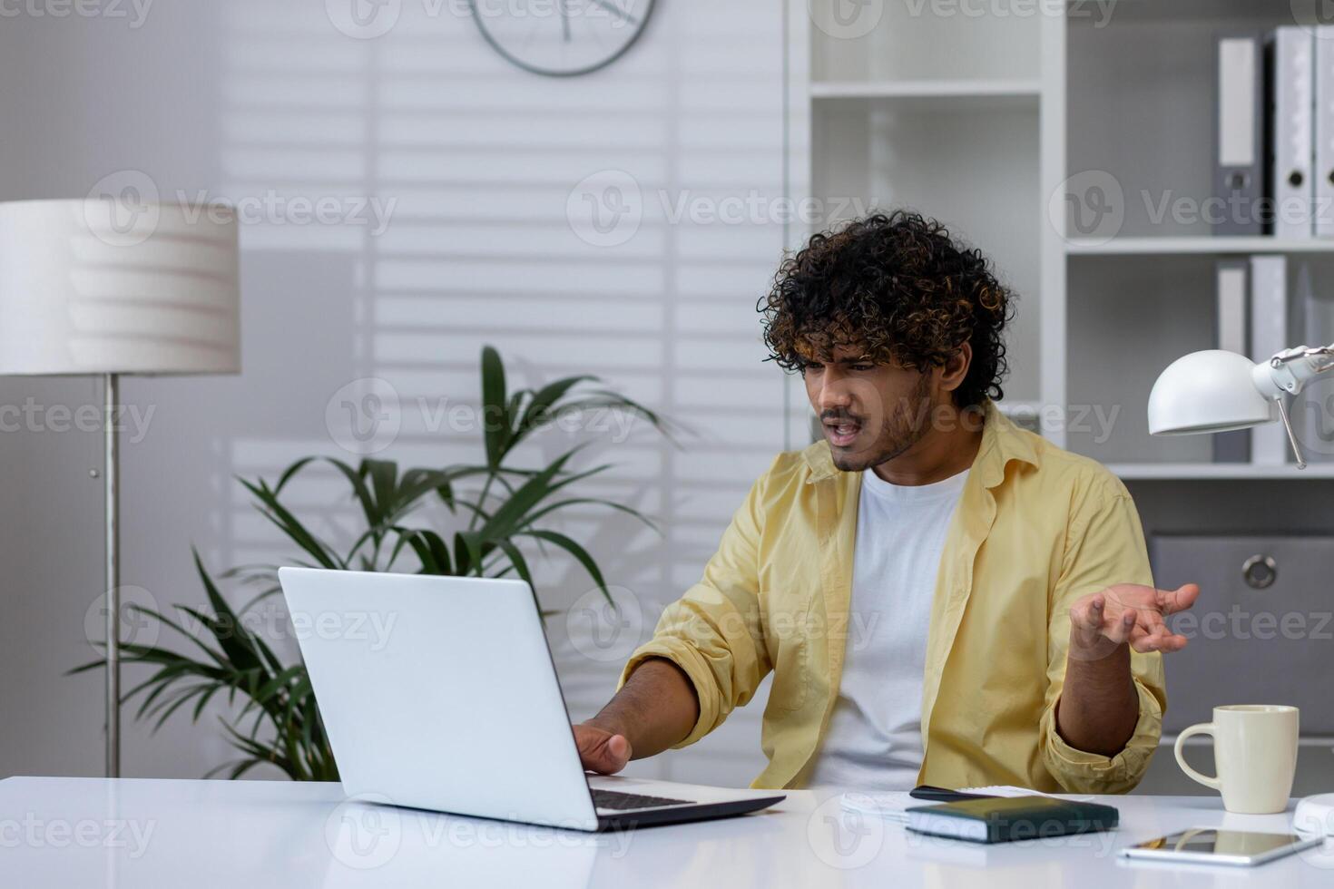 Young man expressing frustration while working on a laptop in a contemporary office environment. The scene captures a stressful moment during a workday. photo