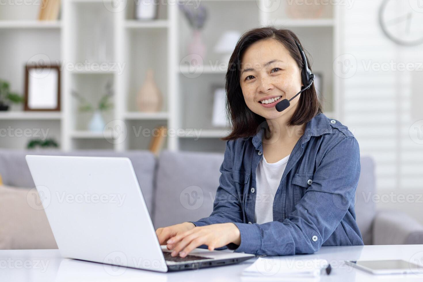 Smiling woman working from home wearing headset in a bright, modern office space with a laptop and notebook. Perfect for illustrating remote work, online communication, and customer support. photo