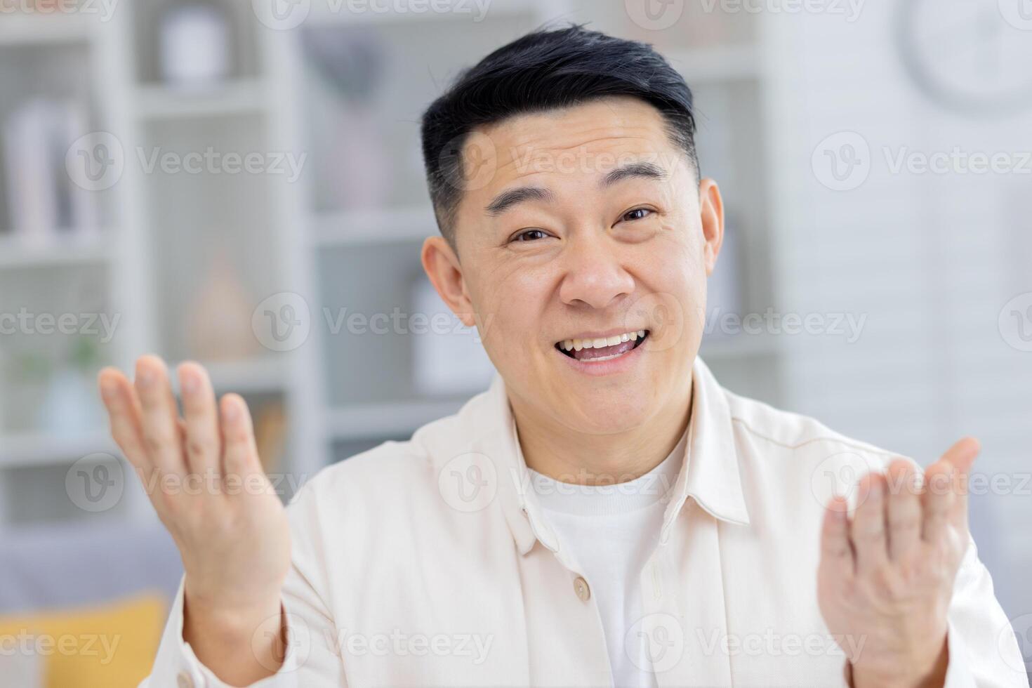 A mature Asian man enjoys a lively call from his modern living room. His hands are raised expressively as he communicates happiness, image captures engagement during the casual conversation. photo