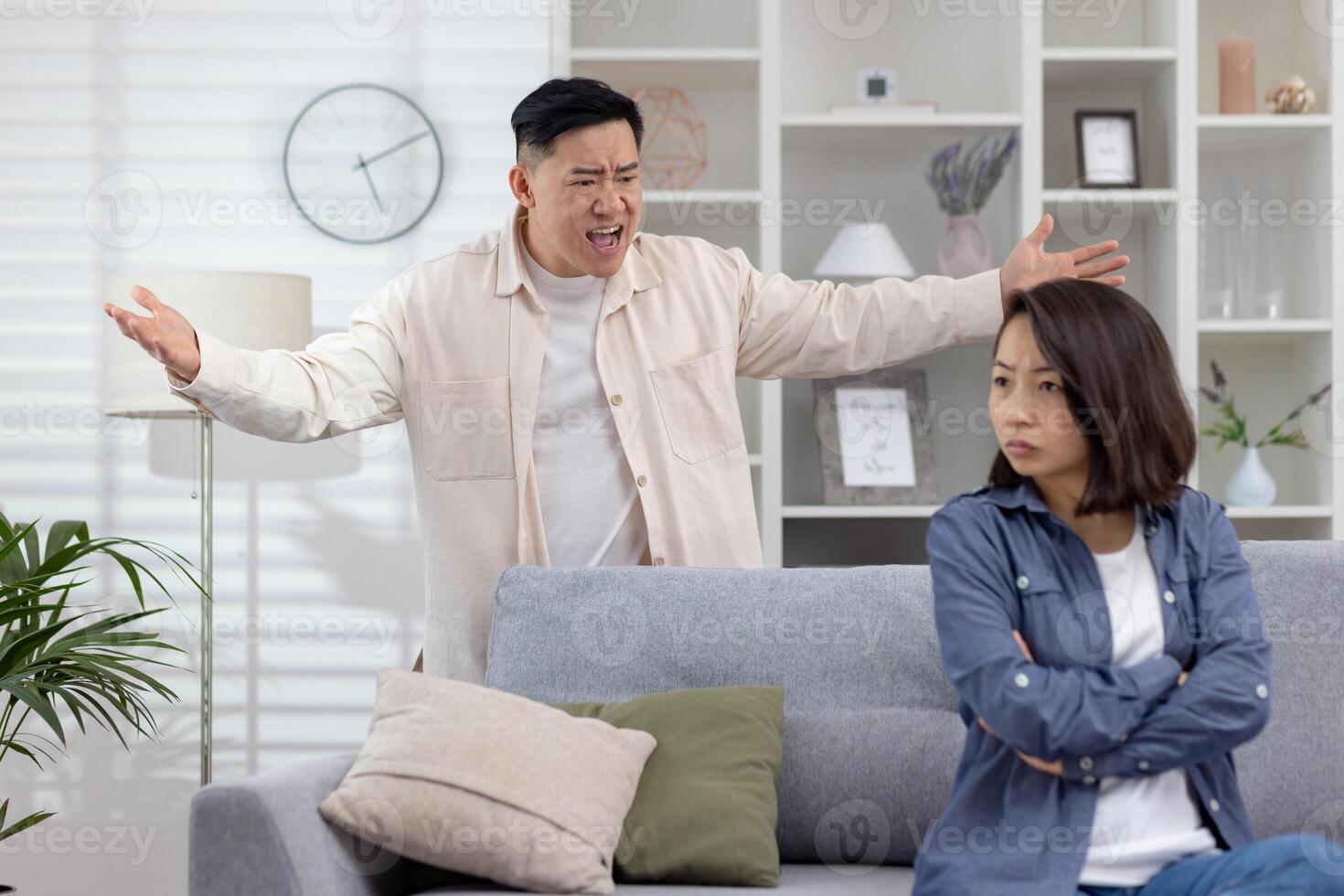 Man upset and yelling, gesturing with frustration, while a woman sits calmly appearing indifferent or tired of the argument. The setting is a modern living room , photo