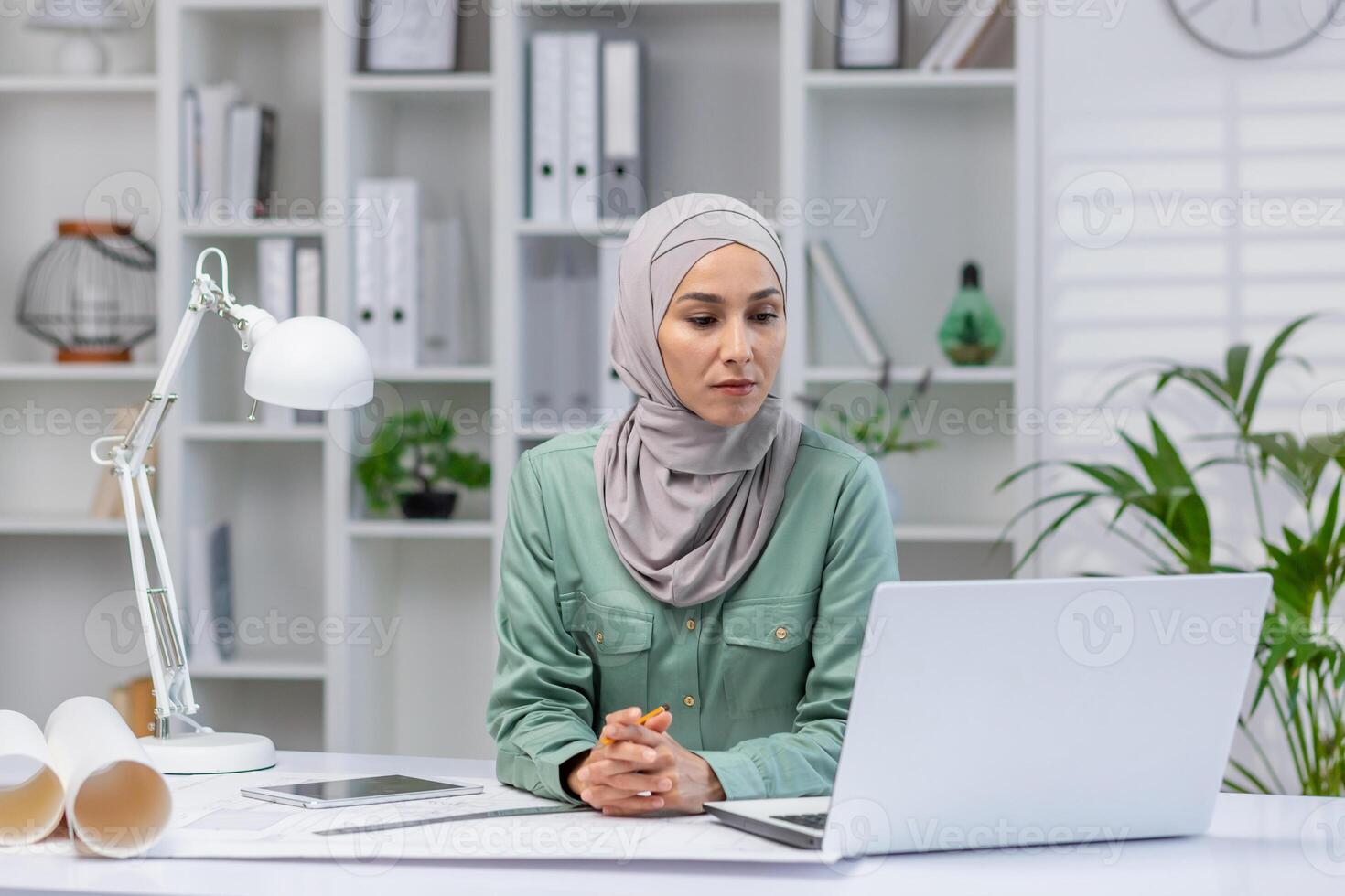 Woman in hijab designer working in home office, architect using laptop at work, studying technical assignment online, serious and concentrated reading. photo
