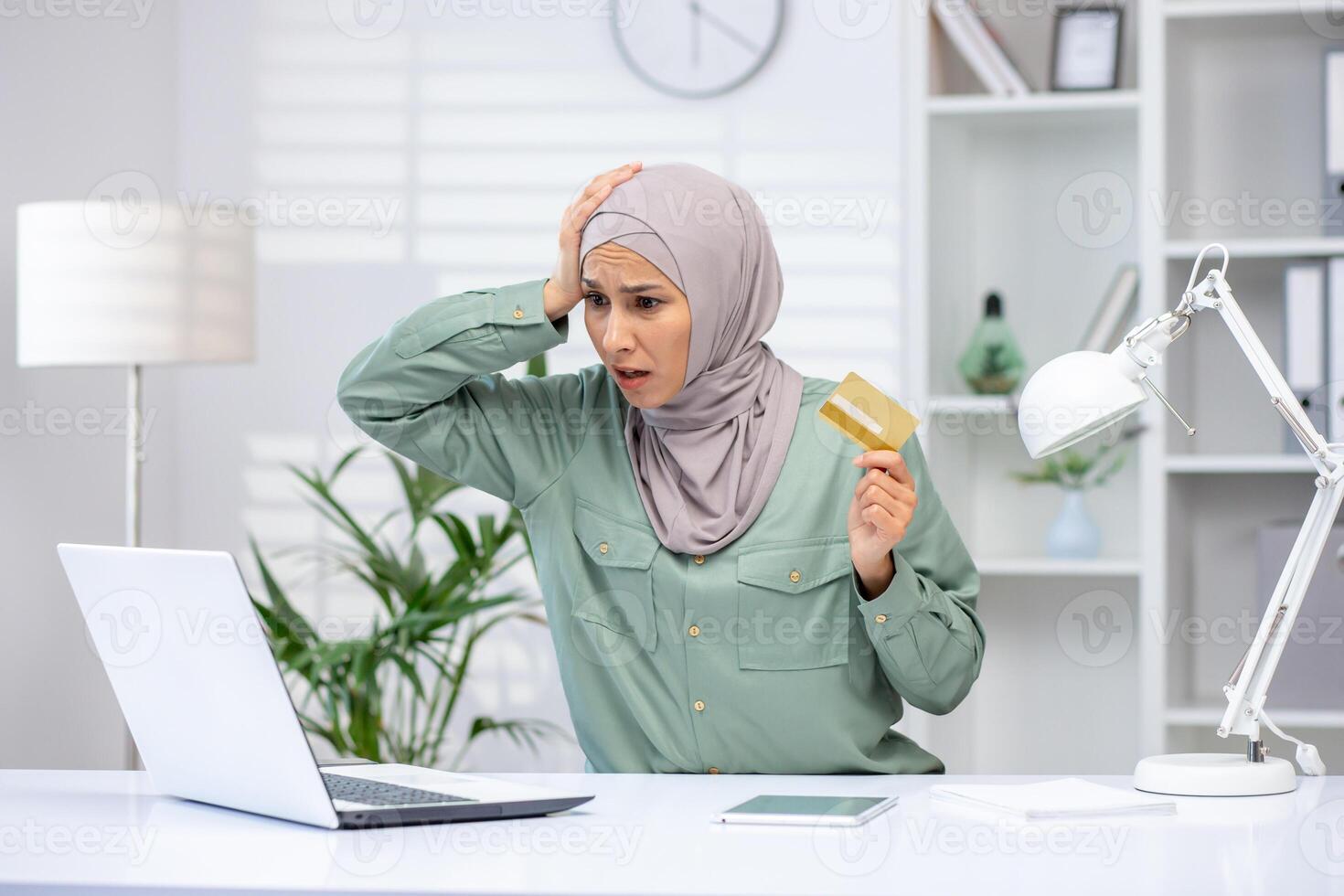 Deceived woman in hijab trying to make an online purchase, business woman holding bank credit card, rejected money transfer error, fraudulent actions. photo