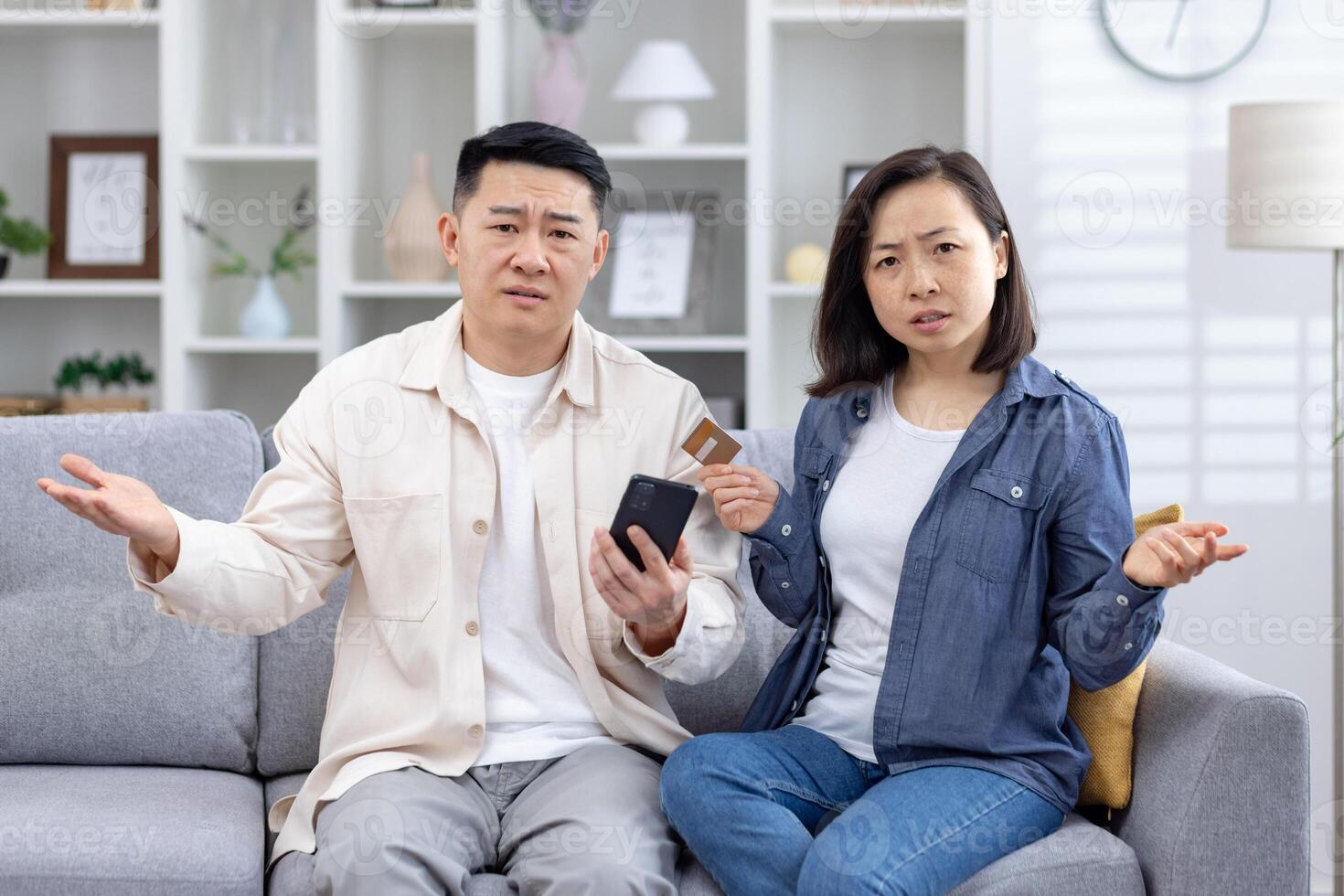 Confused couple sitting on a couch with a smartphone and credit card, facing online payment issues. They appear frustrated and puzzled. photo