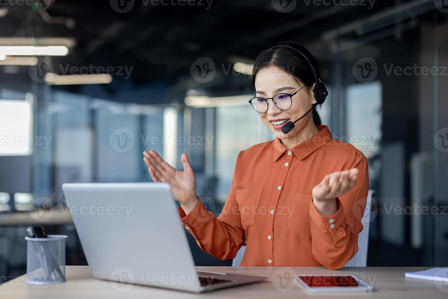 Smiling businesswoman wearing a headset, participating in an online meeting using a laptop at a modern office. Professional communication and teamwork concept. photo