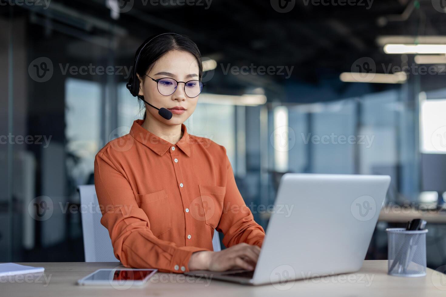 Call center agent wearing a headset while working diligently on a laptop at a modern office desk. Professional work environment. photo