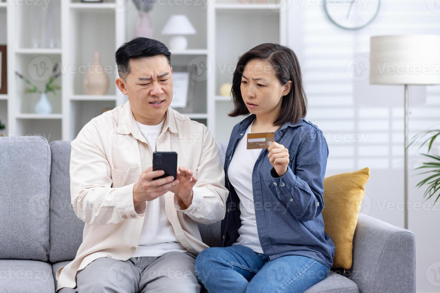 Asian couple looks distressed as they uncover unauthorized charges on their credit card phone, man confusion while the woman, holding the card, seems anxious. stress, frustration of financial fraud. photo