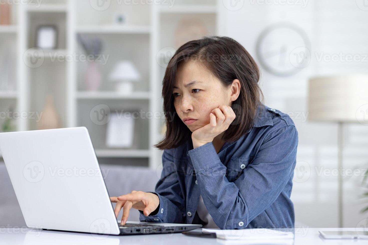 Asian woman looking intensely at a laptop screen while working from home. She epitomizes concentration and dedication in home office, remote work lifestyle and the challenges photo