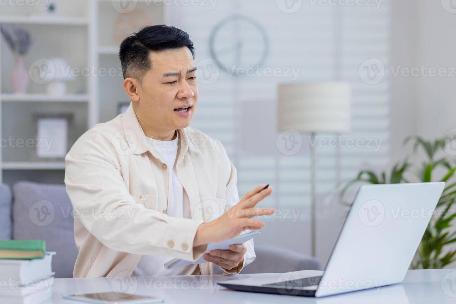 Middle-aged man on a conference call while working from home office, using a laptop, tablet, and books. photo