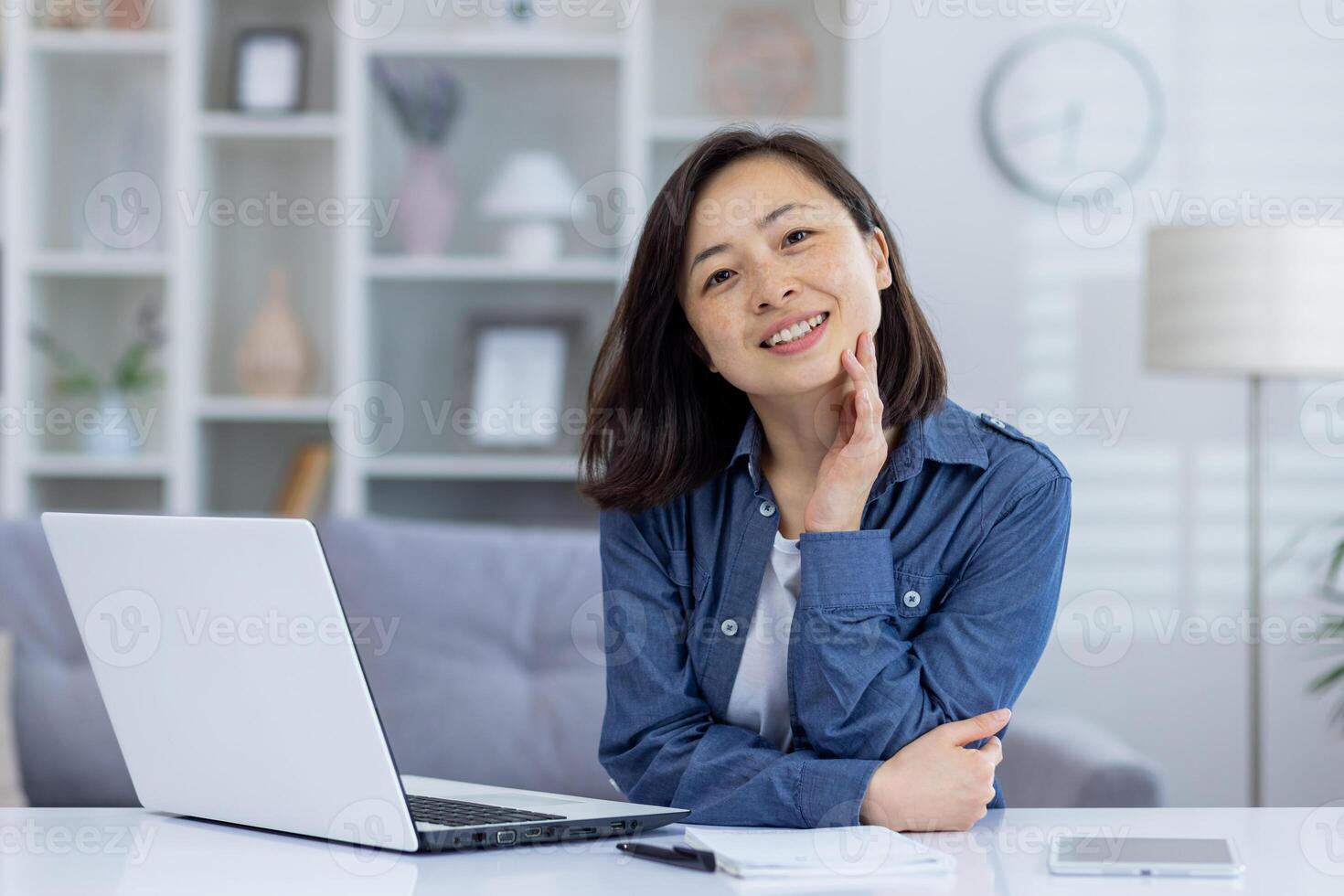 Smiling woman working from home office with laptop, notepad, and mobile device. Cozy home interior in the background. photo