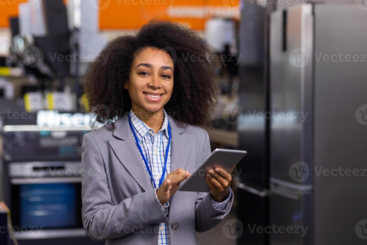 Portrait successful female salesperson in a large home appliance store, an African American woman is smiling and looking at the camera inside a supermarket, holding a tablet computer in her hands. photo