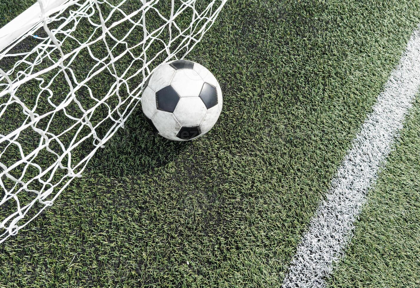 Soccer football in Goal net with green grass field. photo