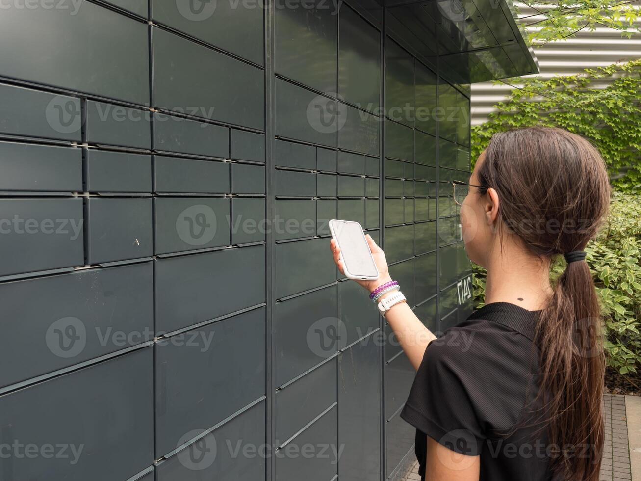 teenage girl opens mail delivery from smartphone. Post terminal machine and parcel delivery. photo