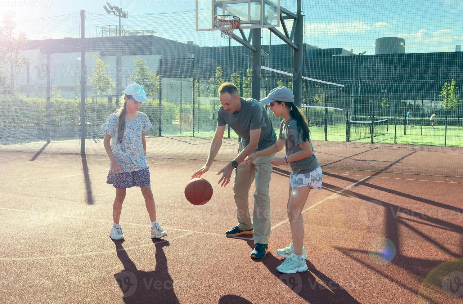 Father and teenage daughters playing basketball outside at court photo