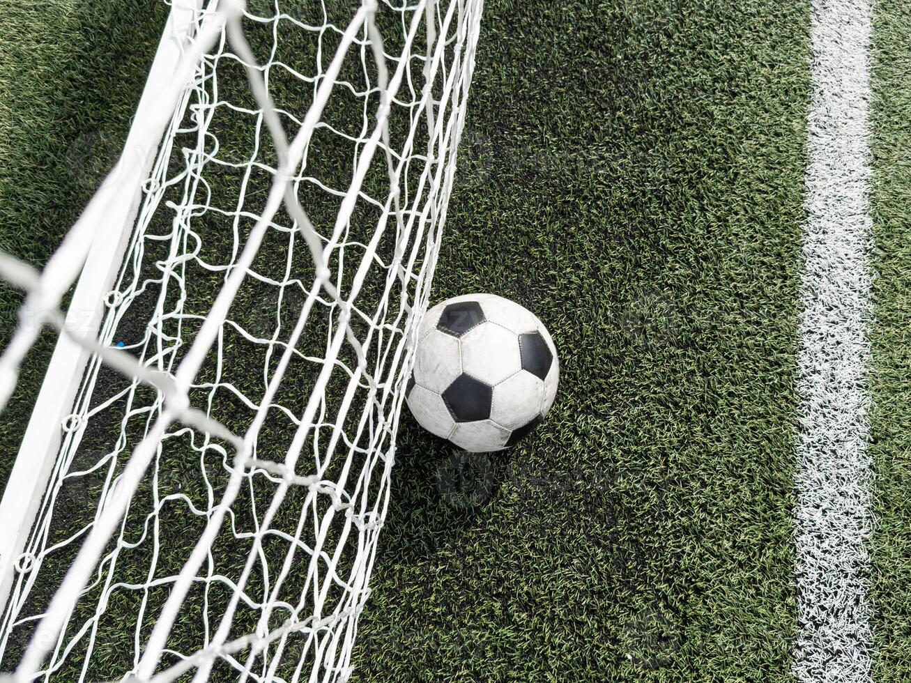 Soccer football in Goal net with green grass field. photo