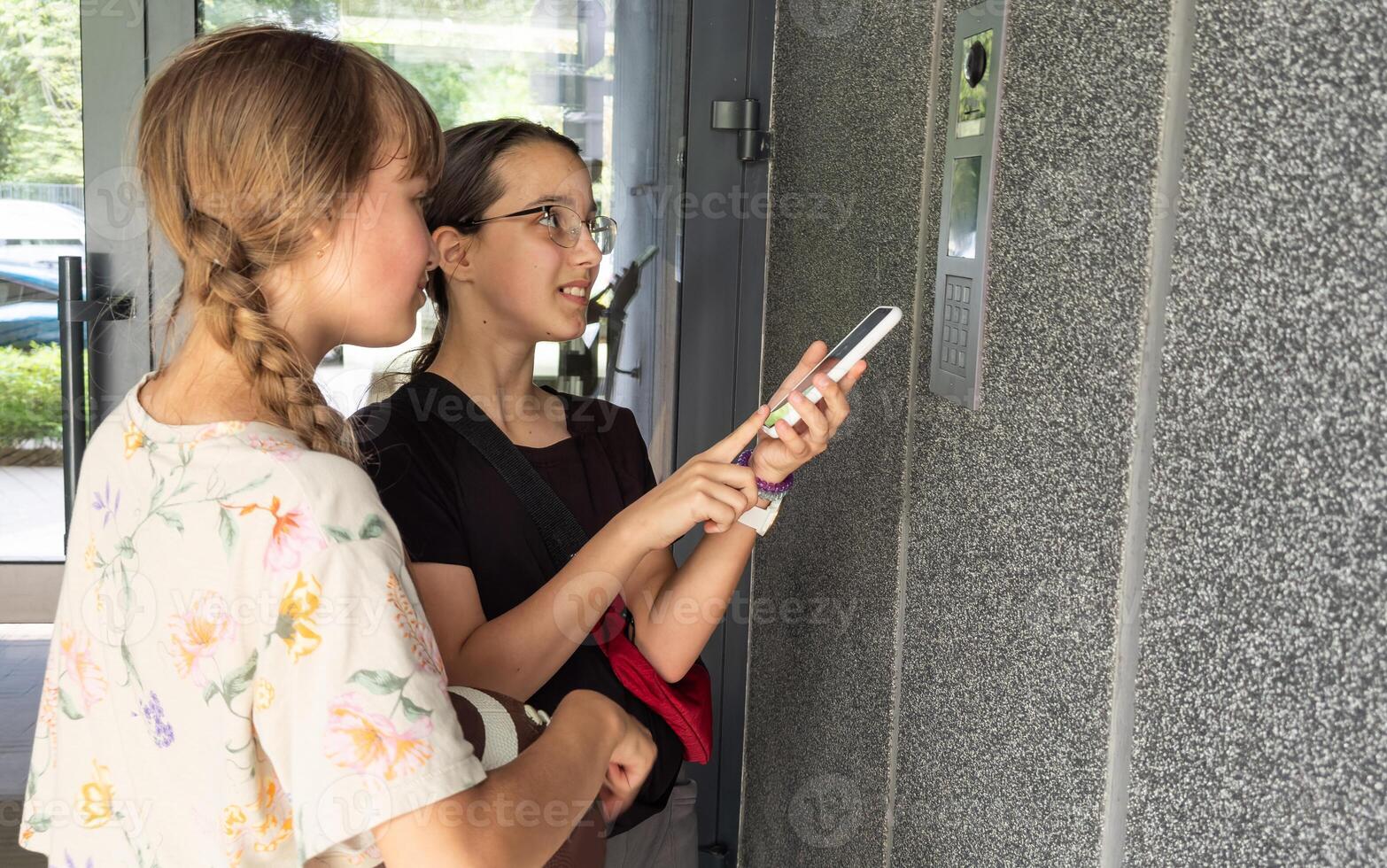 two teenagers getting access to the building by attaching smartphone to intercom. Concept of modern security technologies for access and smart home photo