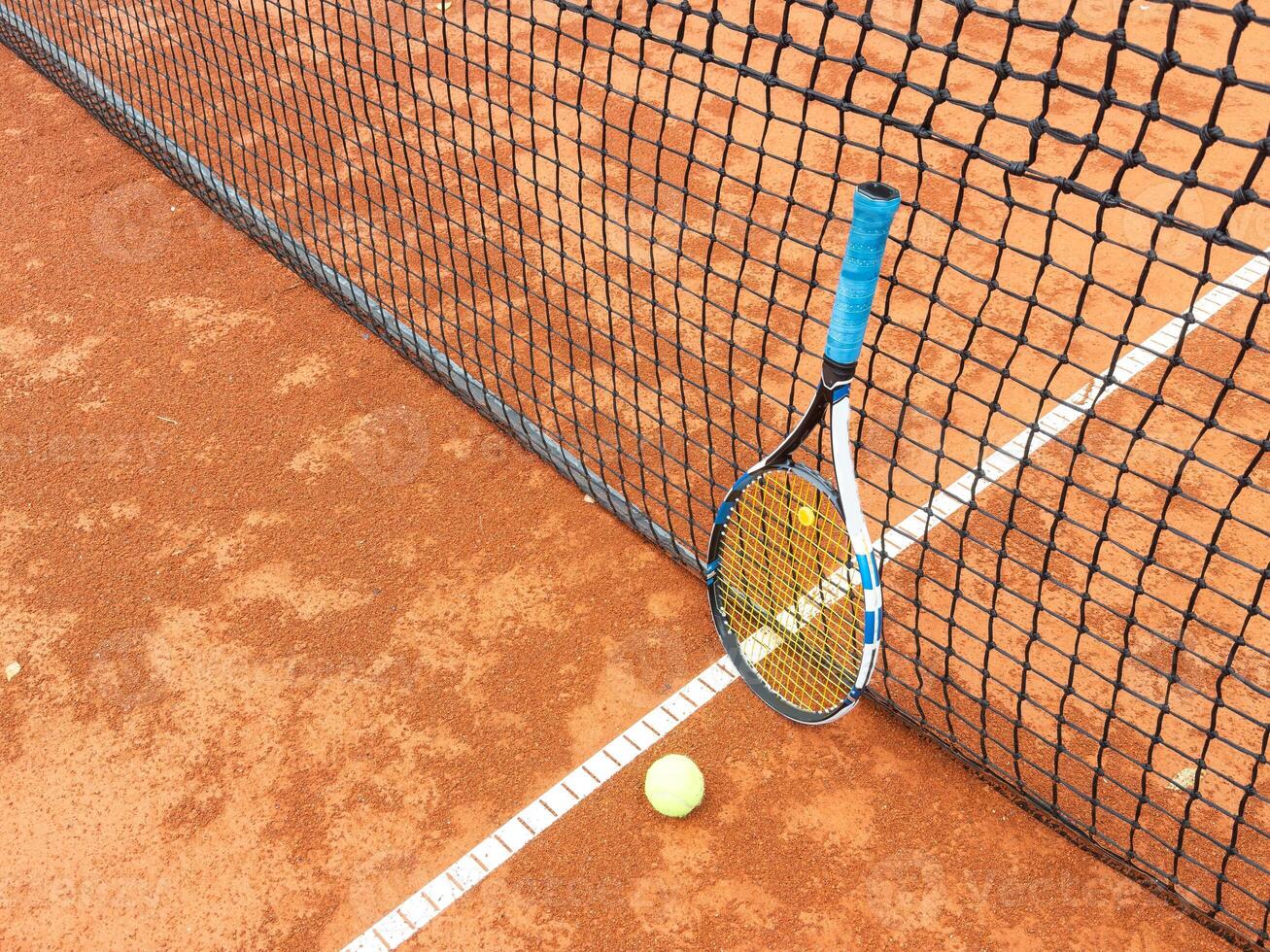 Balls and racket are lying on clay brown professional tennis court Close up of tennis balls and racket on dross at tennis court on the playground. Sport concept. Perspective up top view photo
