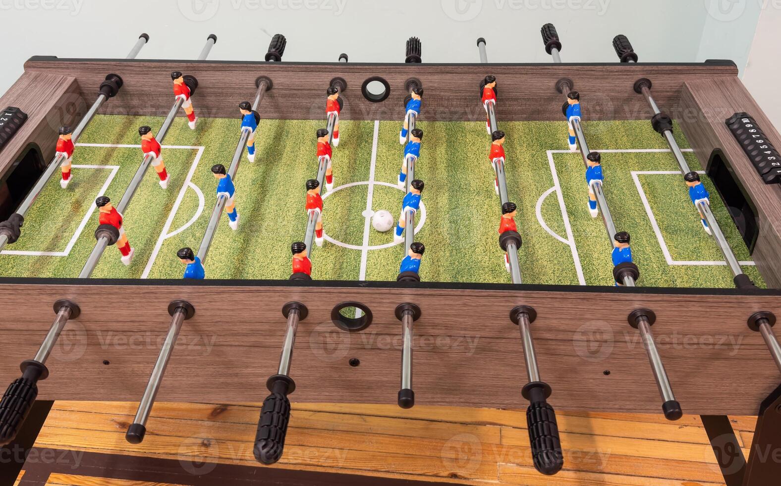 Classic Foosball Table Game With Players in Red and Blue Jerseys During Daytime Indoor Match. Close-up view of foosball table featuring red and blue jersey players positioned for daytime indoor game. photo