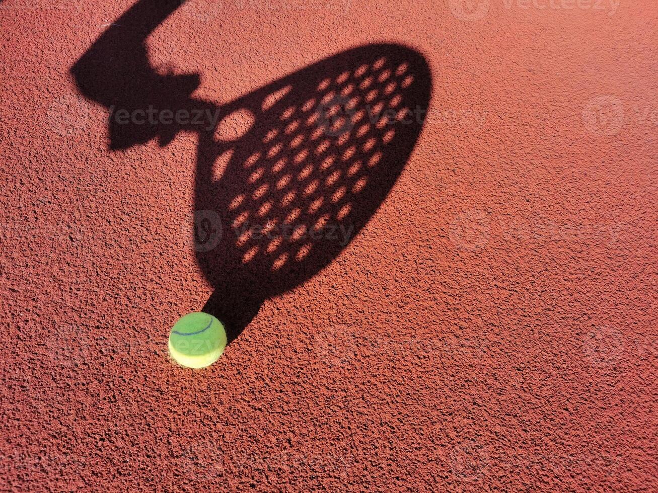 High angle of yellow ball placed on court and covered with shadow of crop person holding padel racket photo