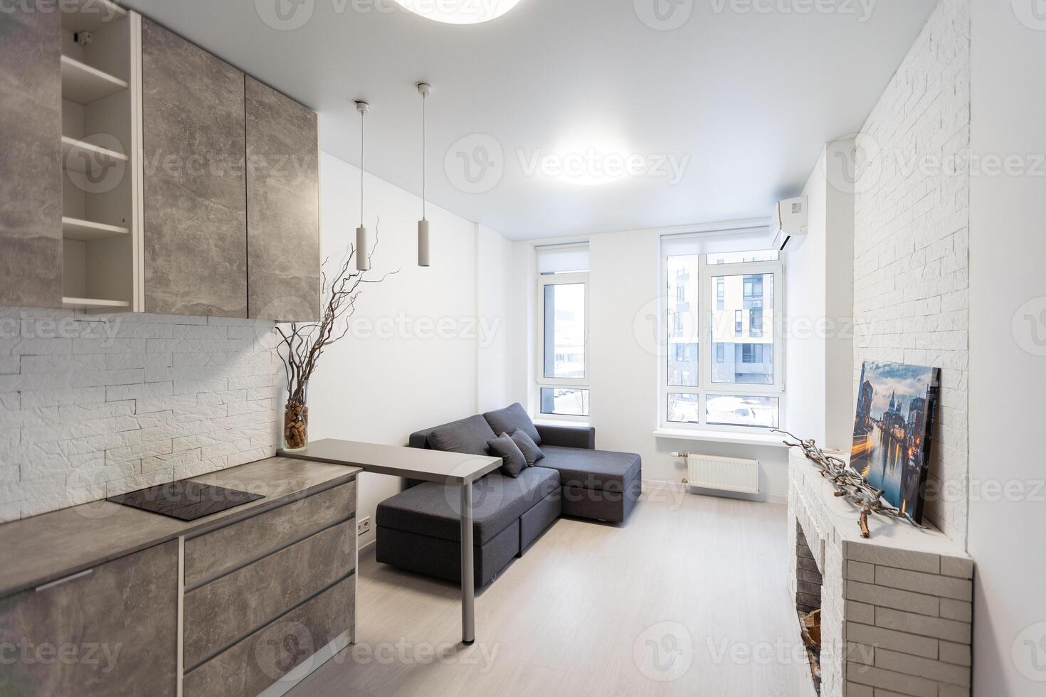 Spacious kitchen with minimalist square shaped furniture, grey floor and walls, counter with integrated sink and pair of bar stools in front of it, built-in microwave and cooktop. photo