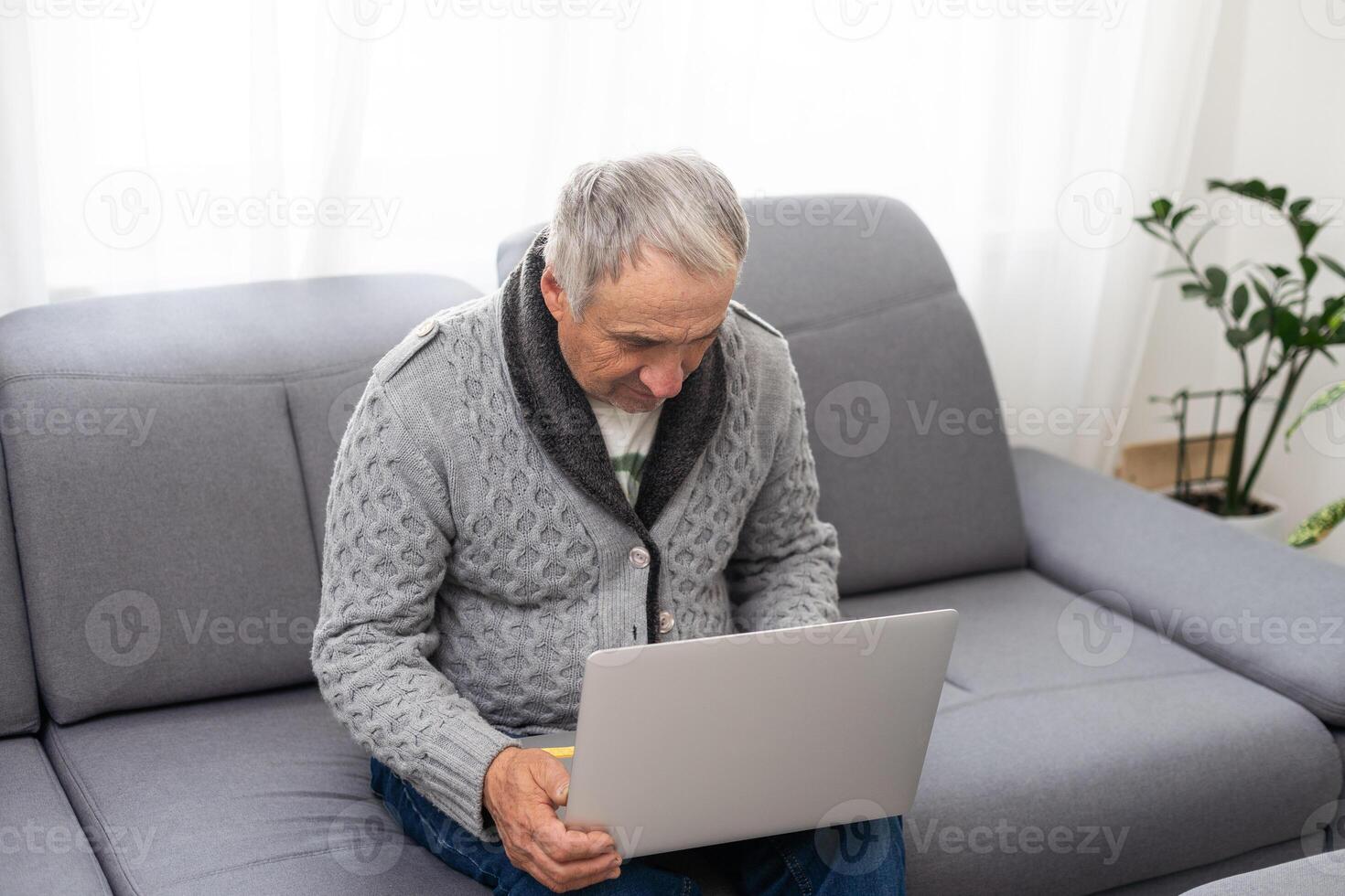 Older man sitting on sofa, smiling at computer screen at home photo