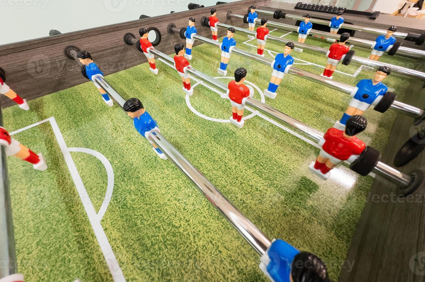 Classic Foosball Table Game With Players in Red and Blue Jerseys During Daytime Indoor Match. Close-up view of foosball table featuring red and blue jersey players positioned for daytime indoor game. photo