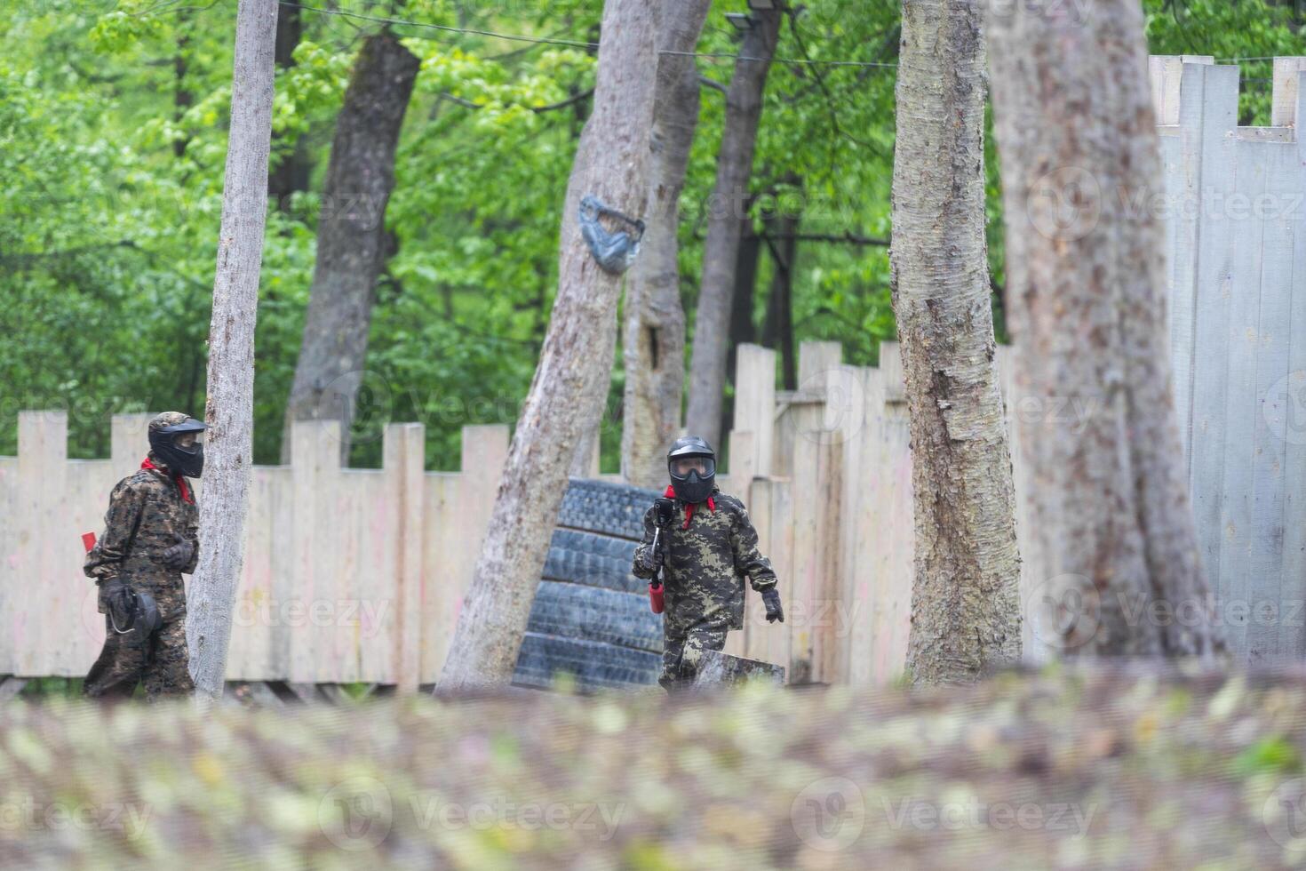 Paintball game. Players with weapons shooting paint balls. Men on the playground. Guys in camouflage and masks are fighting. photo