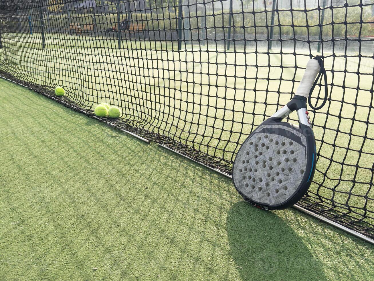 Closeup view of a paddle racket and balls in a padel tennis court near the net. Green background with white lines. Sport, health, youth and leisure concept. Sporty equipment. White lines in background photo