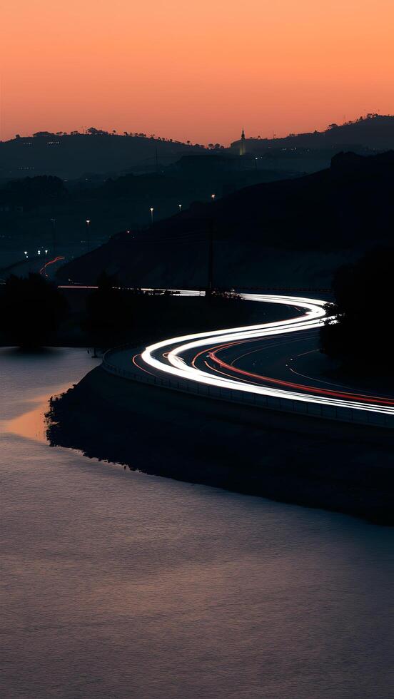 Tranquil scene at dusk calm water, winding road, structures against orange sky Vertical Mobile Wallpaper photo