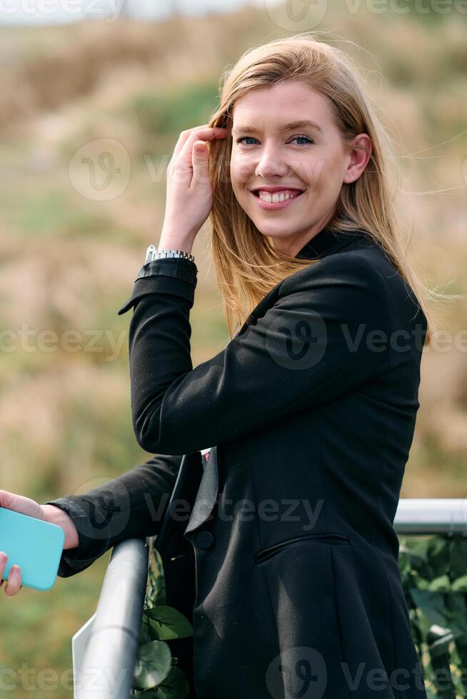 Blonde Businesswoman in Black Suit Using Smartphone on Break in Modern Urban Environment. photo