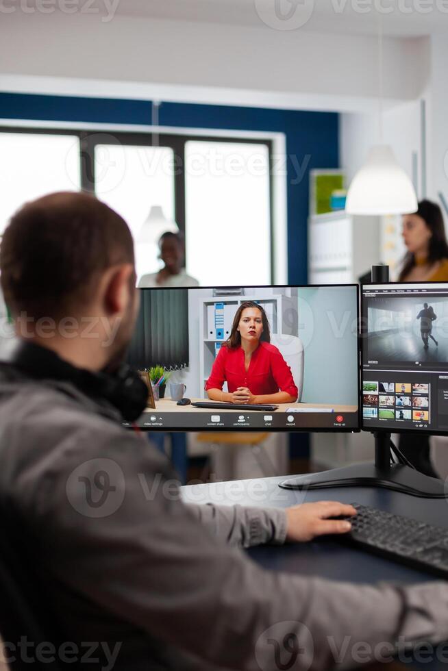 editor talking with remote customer in web online meeting using call editing project, getting feedback on commercial movie using post production program on two displays in creative agency photo