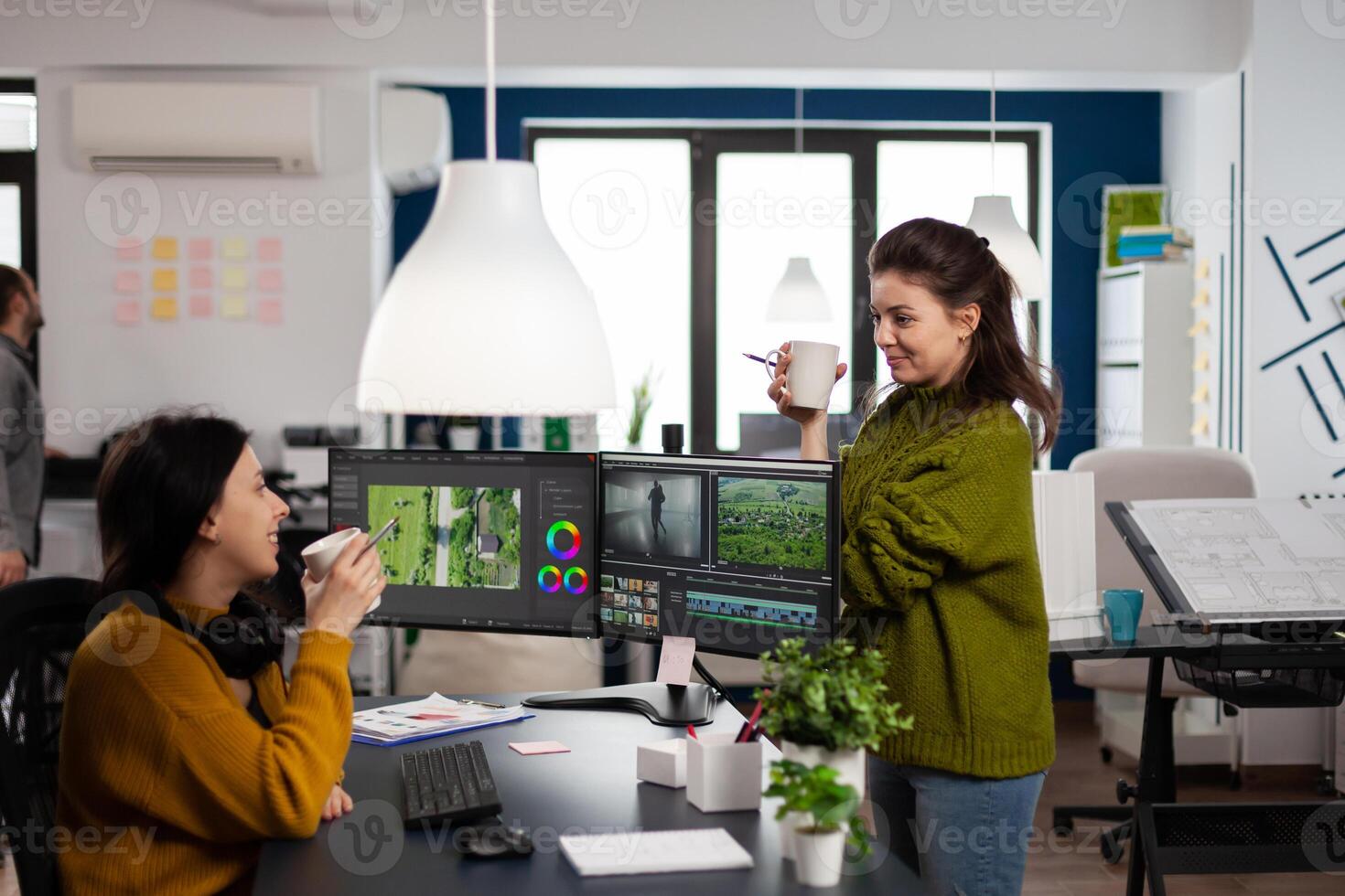 editors discussing holding cups of coffee sharing ideas about developing project of customer in post production software app. Creators women discussing in start up creative agency office photo