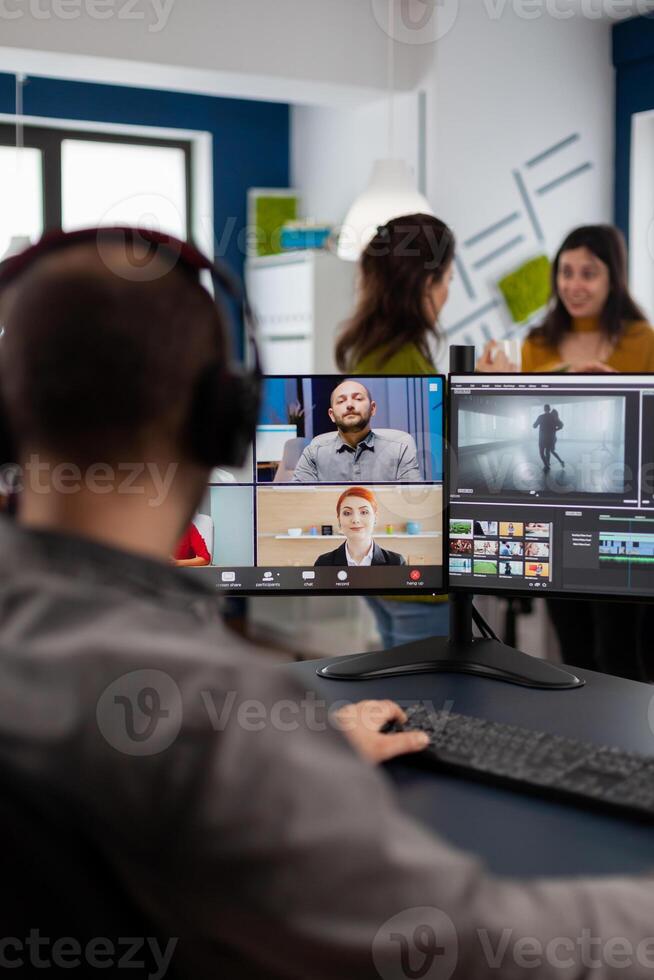 Videographer employee having conference wearing headset editing client movie, getting feedback on commercial project. Freelancer using post production software on pc in creative office. photo