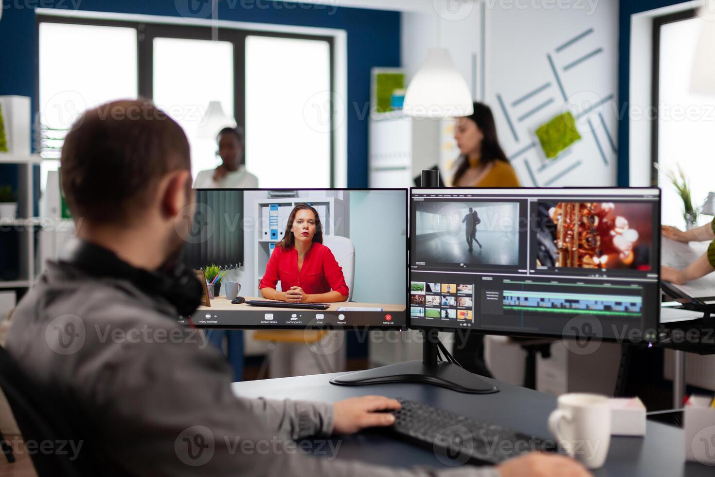 Videographer in web online conference with project manager on call editing client work, getting feedback on commercial movie using post production software on two monitors in start up office photo