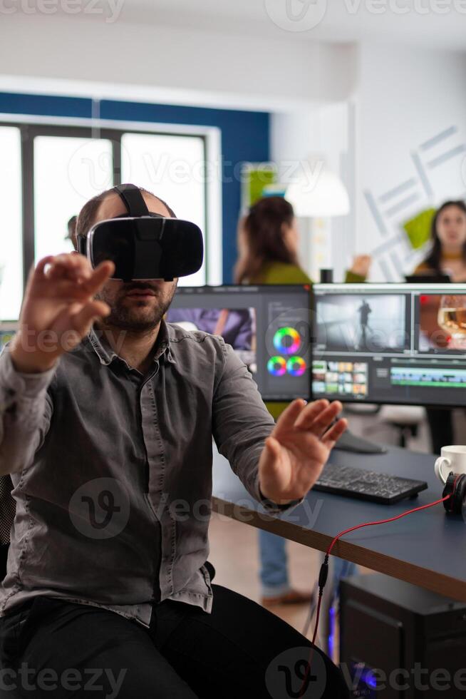 editor experiencing virtual reality goggles prosessing film montage in post production software sitting in creative workplace. Videographer with VR Glasses working in multimedia studio office. photo