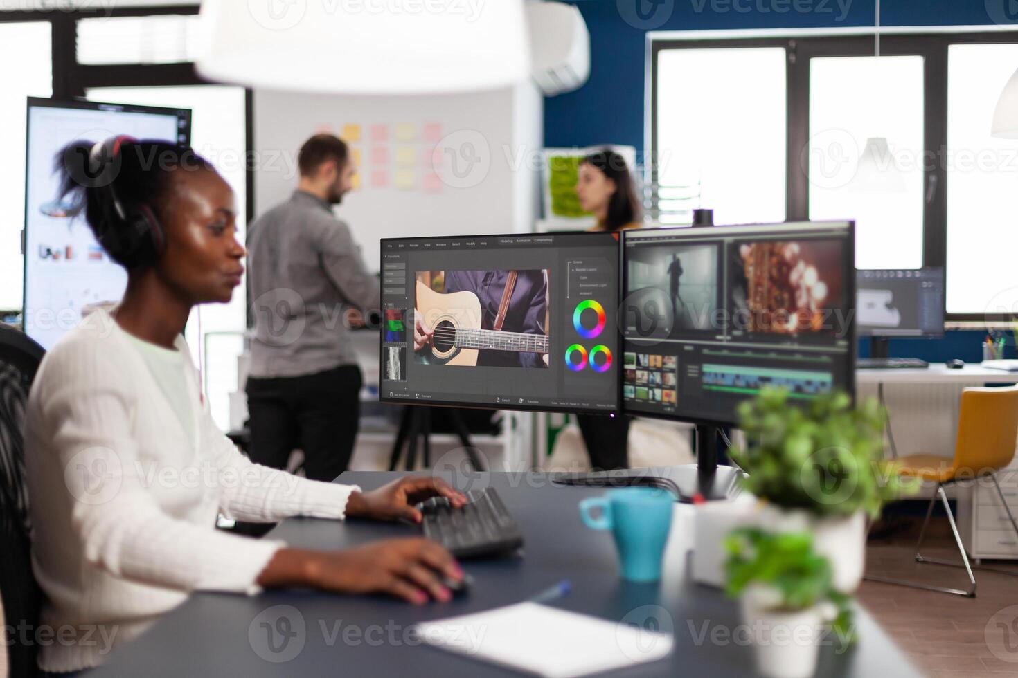 African videographer wearing headset editing movie using post production software working in creative start up agency office. Black editor processing footage on computer with dual displays photo