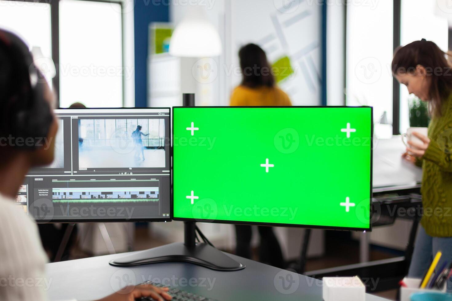 African woman videographer with headset processing film montage working at greenscreen, chroma key isolated display of computer. editor editing movie in post production software in agency office photo