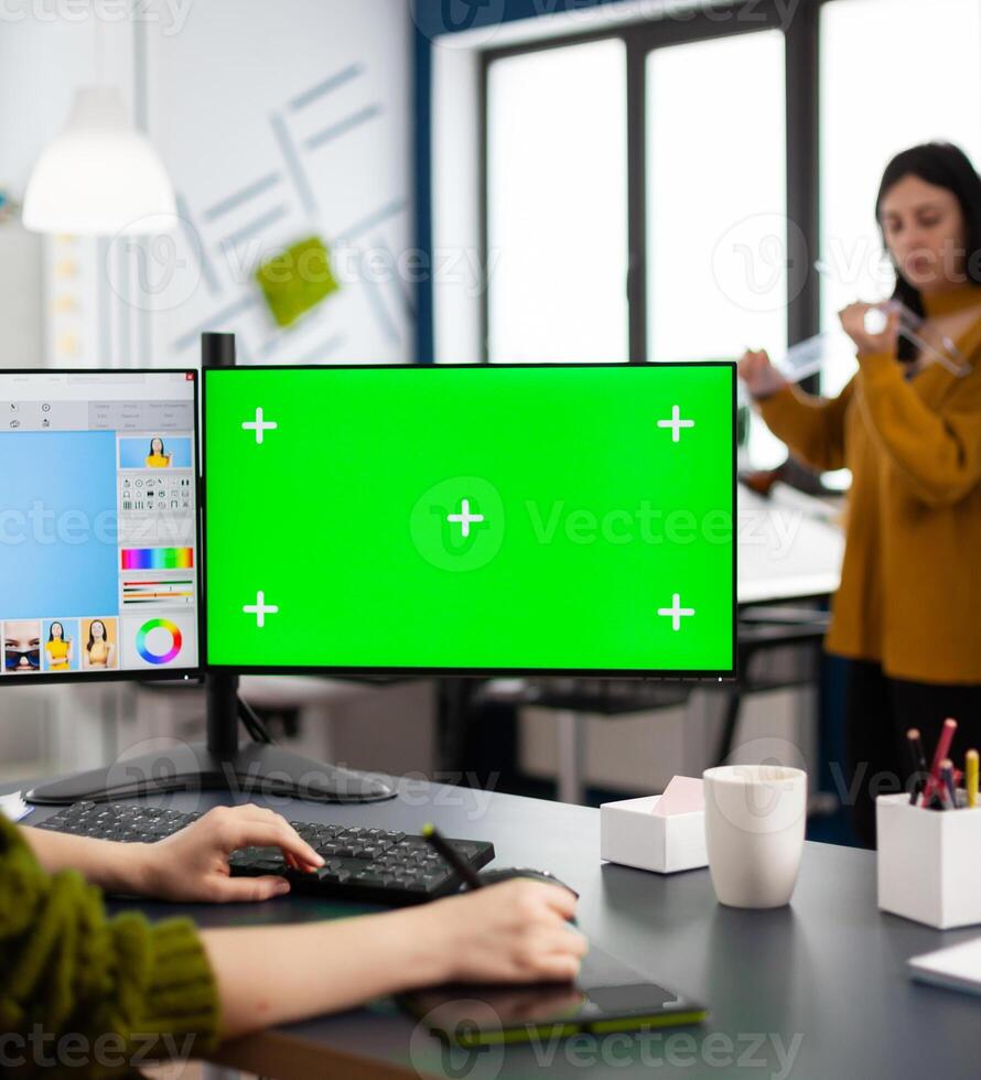 Photographer working on green mock-up screen, computer with chroma key, isolated display while sitting at desk retouching woman portrait in photo editing software. Retoucher looking at greenscreen