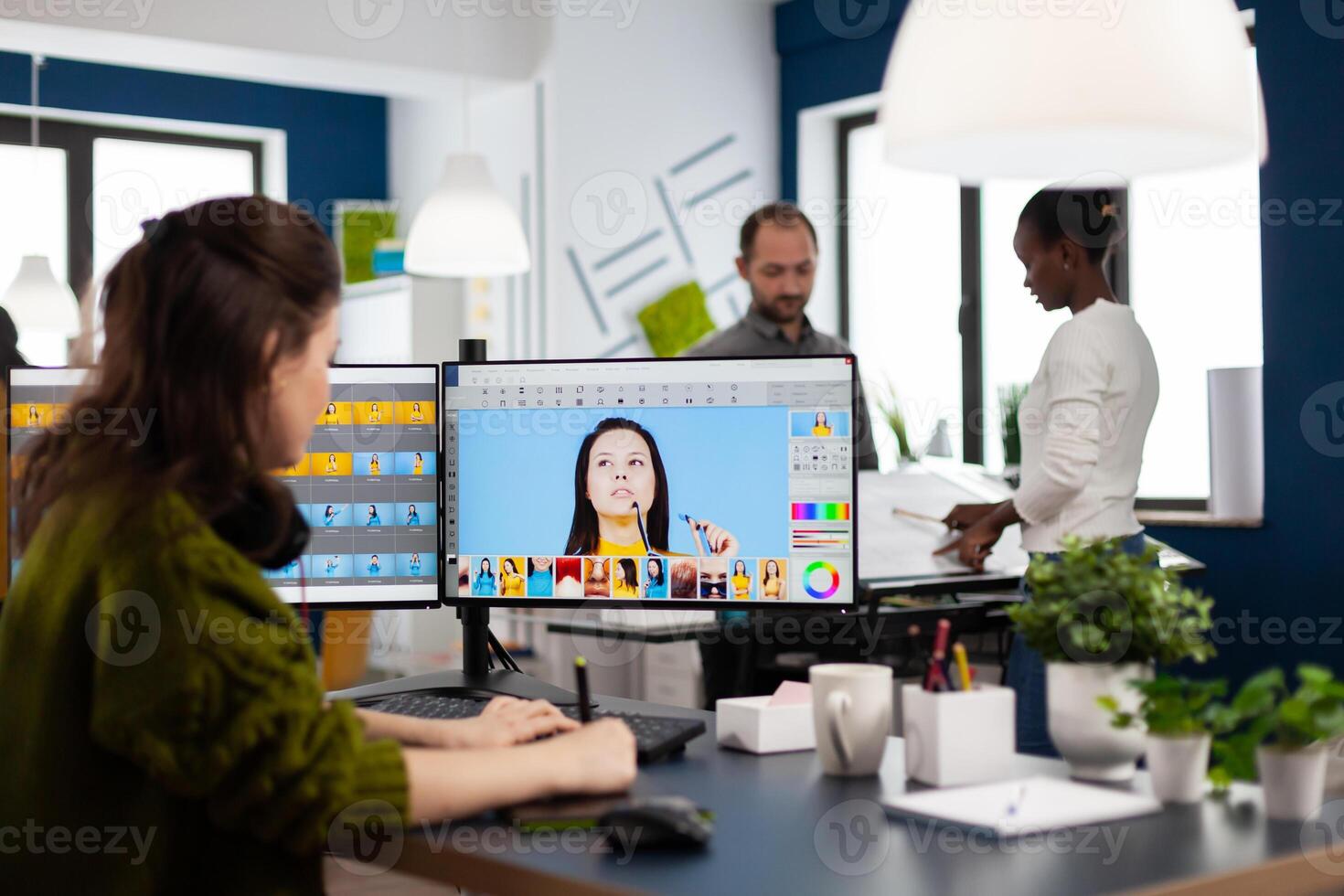 Female photographer edits photos in creative media agency office retouching client imagine with stylus pencil on computer. Freelancer graphic editor working in start up office with digital photos