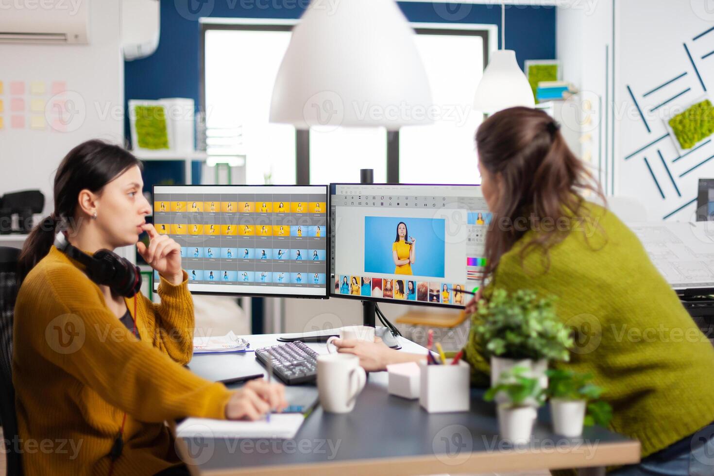 Confident women photo editors sitting at workplace in creative studio retouching photo, art director explaning color greding technic. Retouchers editing with drawing tablet and stylus pencil