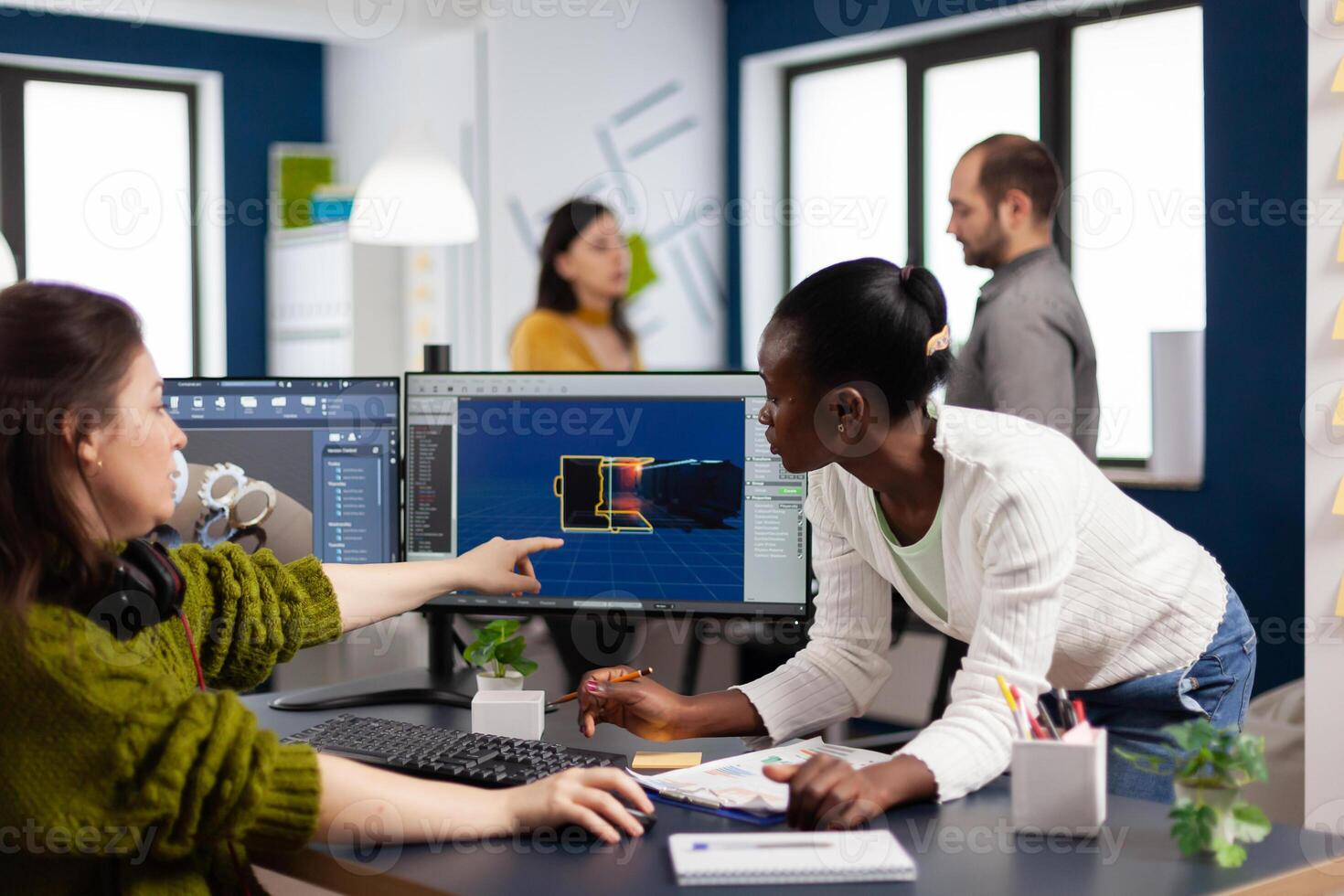 Diverse women game software developers creating game interface sitting in startup creative agency company pointing at pc displays. Workers developing online games with modern technology photo