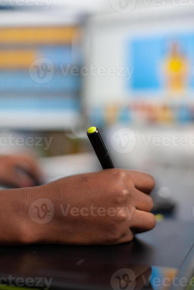 Close up of african photo retoucher holding stylus pen editing customer photo using computer with two displays. Black woman editor retouching assets drawing on graphic tablet in creative agency office