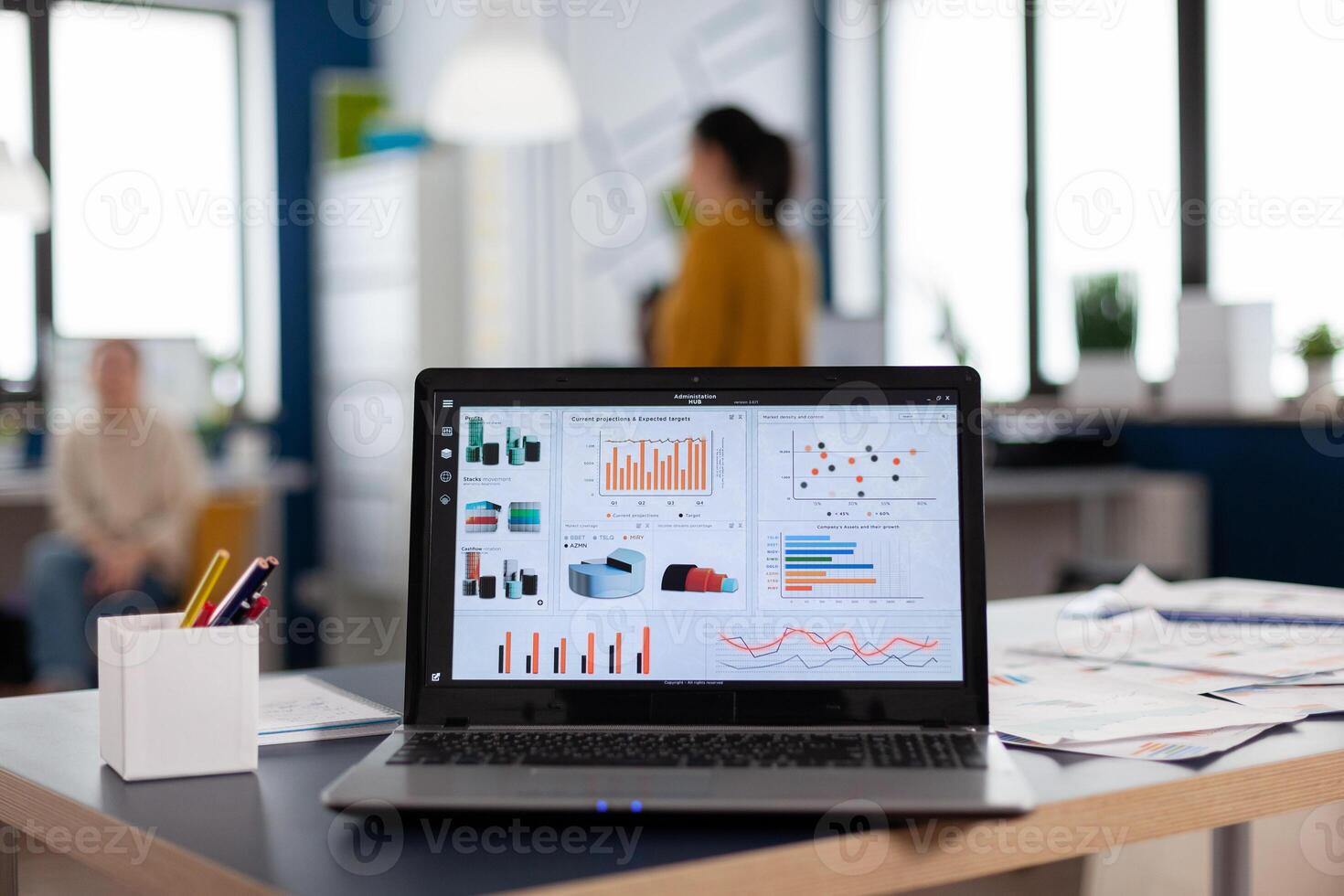 Close up of laptop in start up company office with charts and statistics. Workplace area in business center with multi ethnic employees in it, shot of room with modern furniture and blue wall. photo