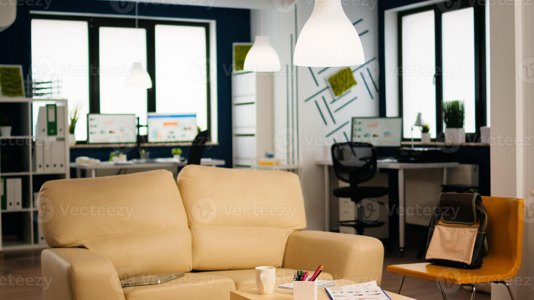 Interior of cozy light company room with small table and confortable couch, modern stylish chairs and desktop computer, all ready for employees. Empty spacious office of creative working space. photo